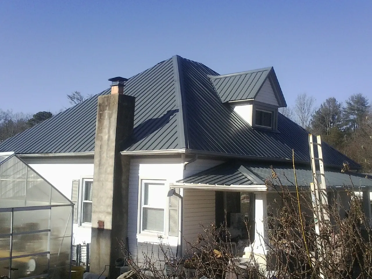 Dark blue standing seam metal roof on a white farmhouse with dormer in Broad Run