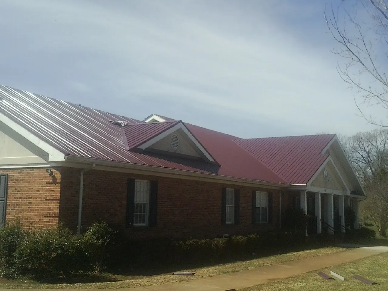 Red metal roof with gabled entries on a long brick building, from a Hail Damage Roof Repair job in Broad Run