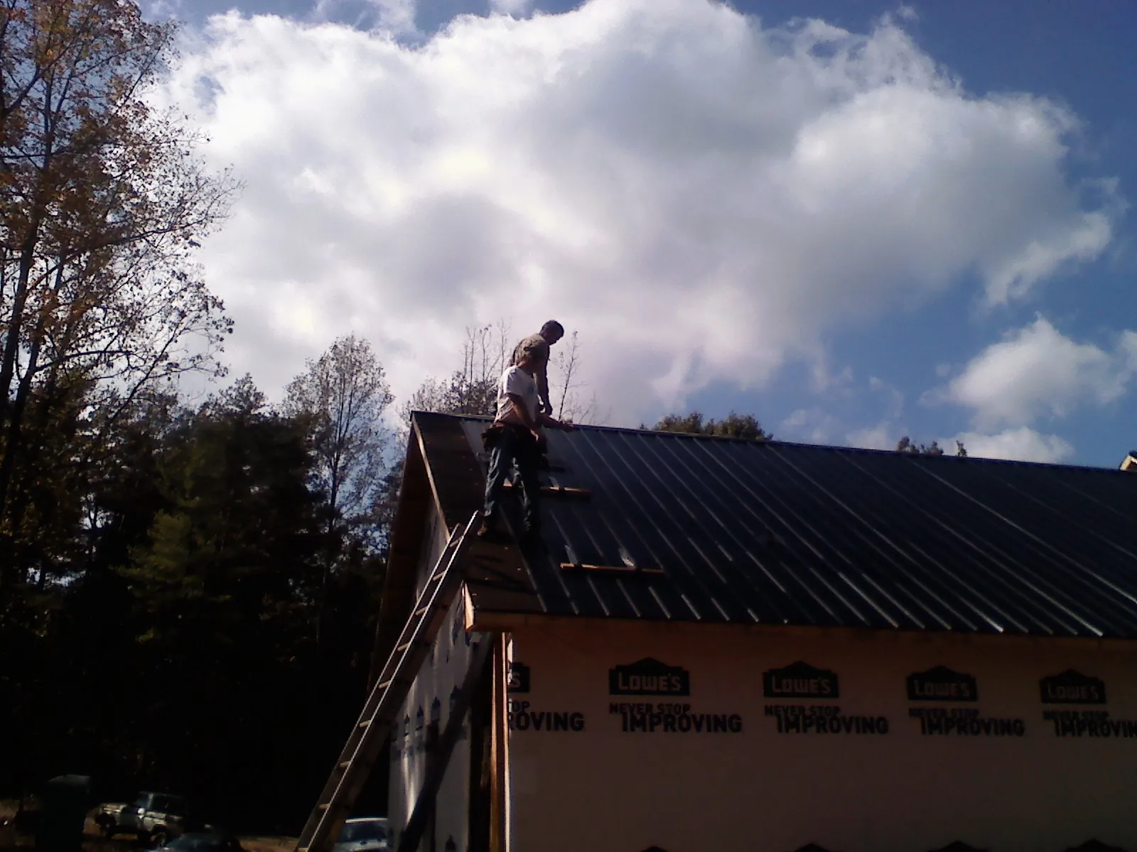 Roofer fastening dark metal panels high against a cloudy sky, from a Roof Inspection job in Broad Run